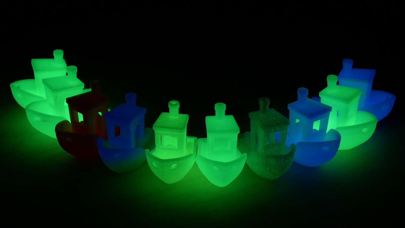 Barcos 3D impresos con filamento Sunlu PLA Glow in the Dark 1.75mm, mostrando efectos de brillo en colores verde y azul en un ambiente oscuro.
